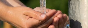 Hände fangen kühles und klares Wasser aus einem Brunnen auf